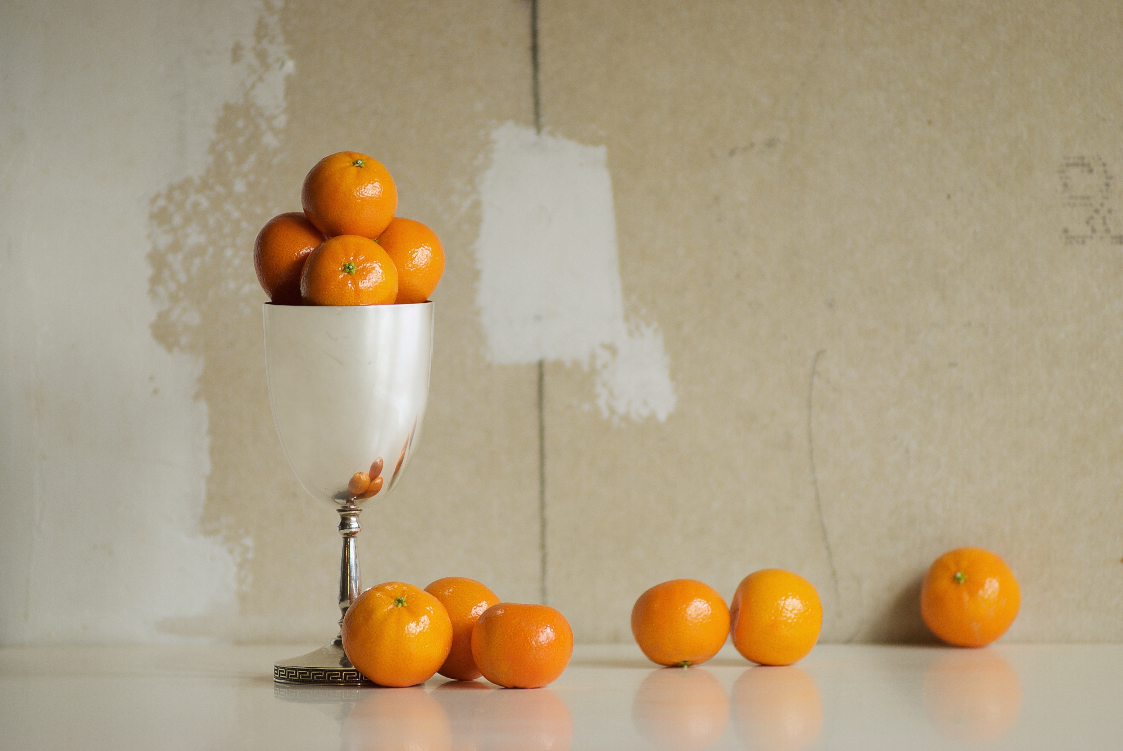 Still life art. Photograph of oranges in a silver goblet against a neutral background in window light.